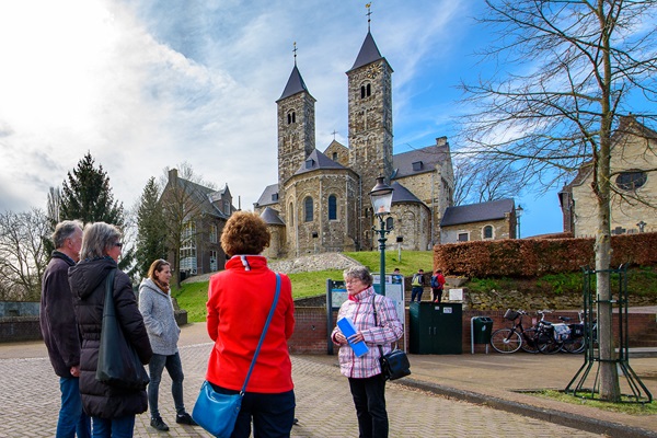 Een gids geeft uitleg aan een groep mensen voor de Abdijkerk in Thorn, een historisch gebouw met twee torens.