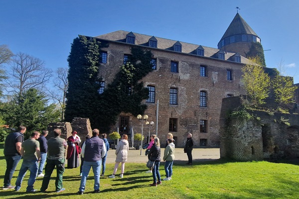 Besichtigung von Schloss Brüggen mit einem Führer in historischer Kleidung und einer Gruppe von Besuchern an einem sonnigen Tag.