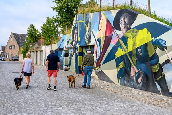 Wandelaars met hondjes lopen langs de street art van Stevensweert waarop de Spaanse veroveraars zijn afgebeeld