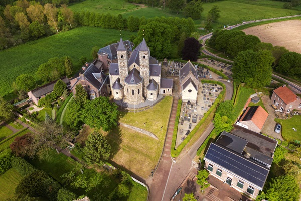 Luchtfoto van de Basiliek van Sint Odiliënberg, een historisch kerkgebouw omgeven door groen, met een kerkhof en enkele gebouwen in de omgeving.