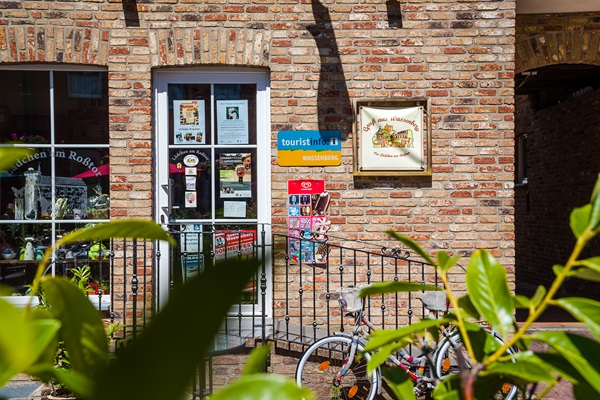 Ingang van het toeristisch informatiepunt in Wassenberg, met folderrek, borden en fietsen voor de deur.