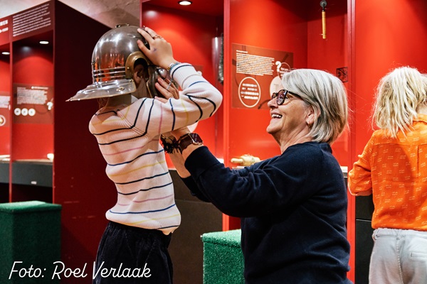 Medewerker van het Museum in Maaseik helpt een meisje met een helm op te doen van een Spaanse ridder