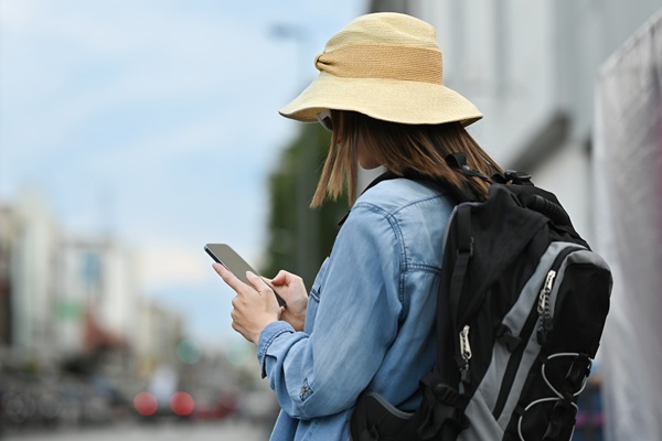 Vrouw met rugzak en hoed bekijkt haar smartphone tijdens een wandeling door de stad.