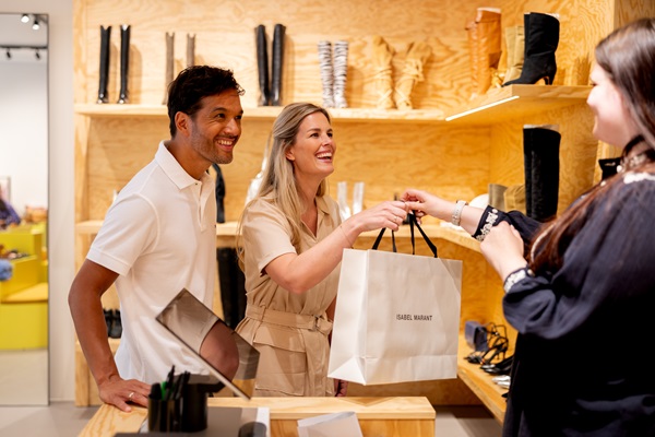 Einem Paar wird von einer Verkäuferin in einem Schuhgeschäft im Designer Outlet Roermond eine Einkaufstasche überreicht.
