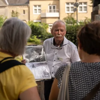 Stadsgids toont historische foto’s tijdens een stadswandeling in Roermond, terwijl twee deelnemers luisteren.